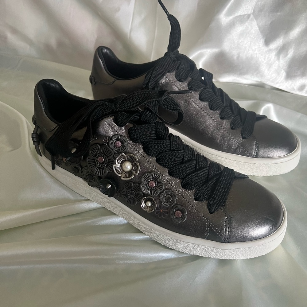 Coach grey metallic leather sneaker with flower accents.